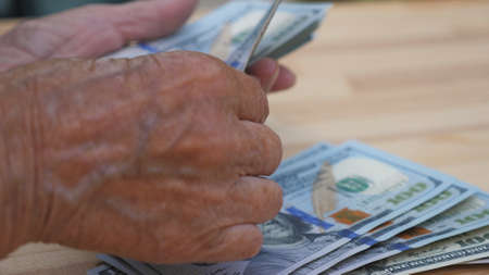 Close up of wrinkled female arms foreign currency and counts cash over the desk. Hands of elderly...