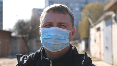 Portrait of man with medical face mask stands at city street during COVID-19 epidemic. Guy wearing...