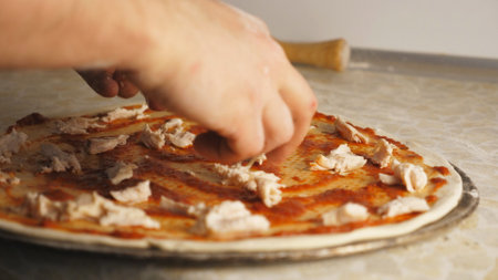 Male hands putting pieces of boiled chicken on the dough in metal form at kitchen. Arms of cook adding ingredient on pastry for preparing tasty pizza at restaurant. Concept of cooking food. Close upの写真素材