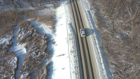 Following to white SUV riding through snowy rural road. Car driving at beautiful countryside route on wintry day. Winter holidays journey at nature. Concept of family travel. Aerial shot Top Viewの写真素材