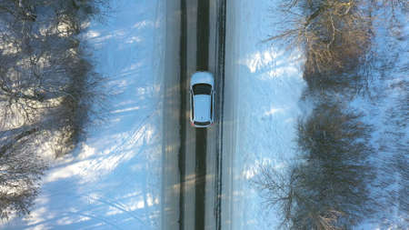 Close up of white car riding through snowy forest road. SUV driving at beautiful countryside route on wintry day. Winter holidays journey at nature. Concept of family travel. Aerial shot Top Viewの写真素材