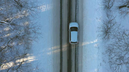Close up of white car riding through snowy forest road. SUV driving at beautiful countryside route on wintry day. Winter holidays journey at nature. Concept of family travel. Aerial shot Top Viewの写真素材