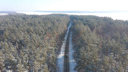 Aerial shot of white SUV going on a snow covered forest road. Car rides at icy woods route at winter time. Auto driving over beautiful nature way. Concept of travel and active weekends. Above viewの写真素材