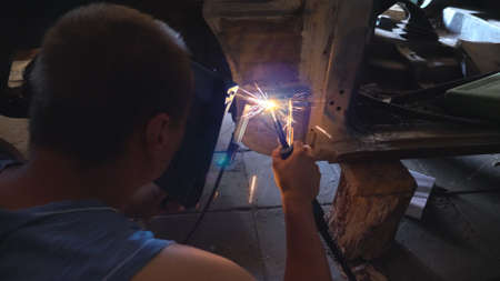Repairer wearing protective mask welding some auto detail. Mechanic working at garage or workshop....