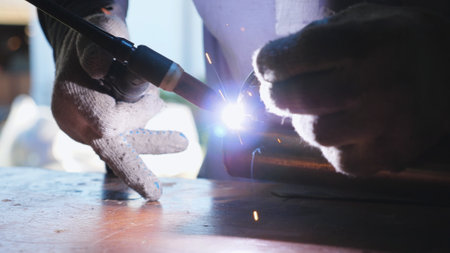 Male hands of repairer in gloves doing welds work using professional equipment. Arms of mechanic welding metal part of auto with soldering iron in workshop. Maintenance service concept. Dolly shotの写真素材