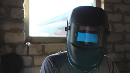 Repairman in gloves holding soldering iron and preparing to weld metal details in garage. Male welder in protective mask ready to work in workshop. Concept of maintenance service. Crane shot Close upの写真素材