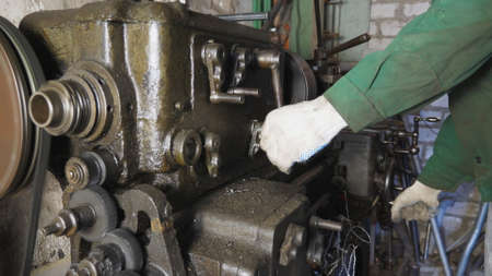 Male hands of mechanic in gloves working on old workbench in his garage. Repairman uses turning lathe to processing metal in workshop. Hard job on milling machine at workplace. Close up Slow motionの写真素材