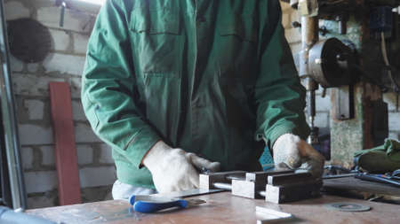 Male mechanic in workwear fixing some metal parts on table at garage. Young repairer working at...