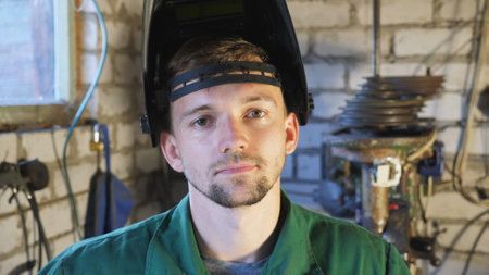 Portrait of tired young repairman with open protective mask on his head looking into camera in his garage. Professional mechanic in workwear working in workshop. Maintenance service concept. Close upの写真素材