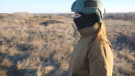 Female ukrainian army soldier walking at the field. Woman in military uniform and helmet going on meadow at sunset. Ukraine victory against Russian aggression. Invasion resistance concept. Slow motionの写真素材