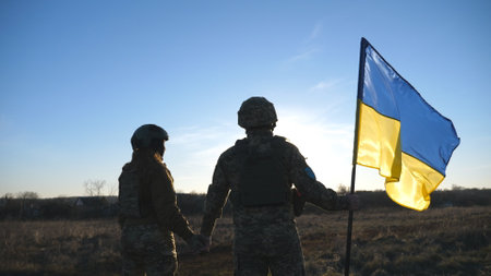 Ukrainian army soldiers stands outdoor at sunset time and waves flag of Ukraine. People in military uniform lifted up flag against blue sky. Victory at war. Resistance to russian invasion. Slow motionの写真素材