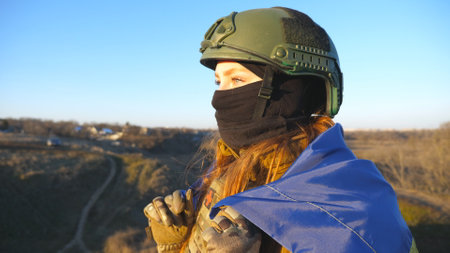 Profile of female ukrainian army soldier stands with flag of Ukraine and looks into the distance. Woman in military uniform and helmet sight with hope to the horizon. Victory against Russia aggressionの写真素材