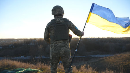 Soldier of ukrainian army runs to the hill top to wave flag of Ukraine. Man in military uniform lifted up flag against sunset as sign of victory against russian aggression. Invasion resistanceの写真素材