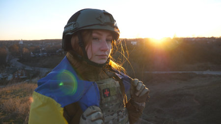 Female military medic of ukrainian army holding flag of Ukraine and looking into camera. Girl in...