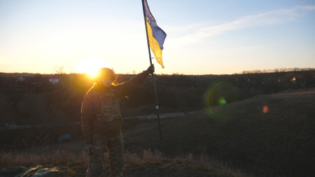 Woman in military uniform stands against sunset and lifted up flag of Ukraine. Female ukrainian army soldier holding waving flag. Victory against russian aggression. Invasion resistance conceptの写真素材