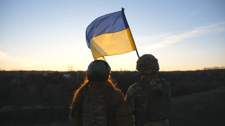 Soldiers of ukrainian army raising flag of Ukraine against background of sunset. People in military...
