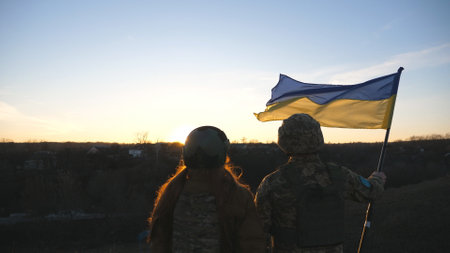 Soldiers of ukrainian army raising flag of Ukraine against background of sunset. People in military uniform lifted up yellow-blue flag. Victory against russian aggression. Invasion resistance conceptの写真素材