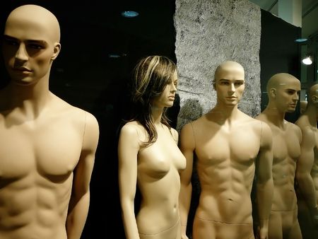 naked mannequins in dark shop window: one woman among menの写真素材