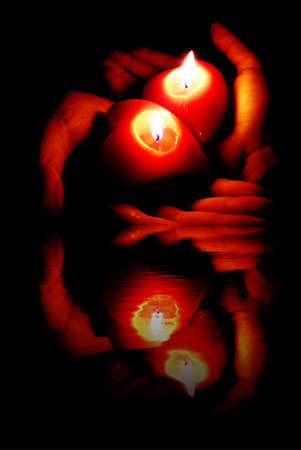 two open palms holding fired -shaped candles, with reflection effectの写真素材