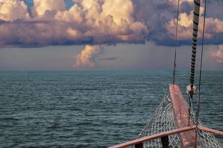 The bow of the ship against the sea horizon with a grid, steel cables and a folded sail. Ancient wooden ship sailing on the seaの写真素材