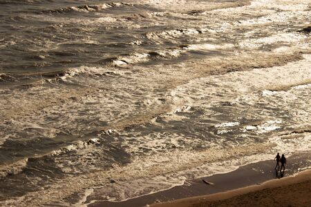 people walk along the evening coast at golden sunsetの写真素材