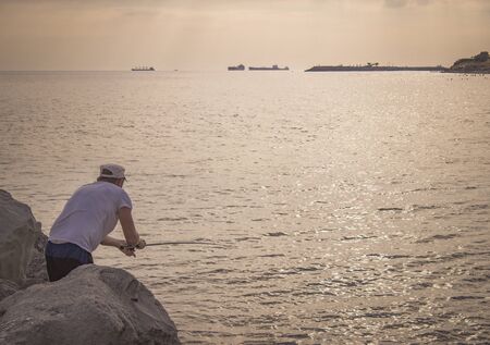 A grown man throws a fishing rod into the sea. Fisherman fishing from rocks and stones in the oceanの写真素材