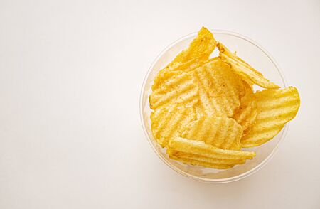 Potato chips in a clear glass. Yellow grooved potato chips in a glass bowl.