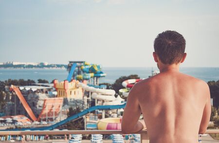 A man with a naked torso looks at a large water Park with water slides. Rear viewの写真素材
