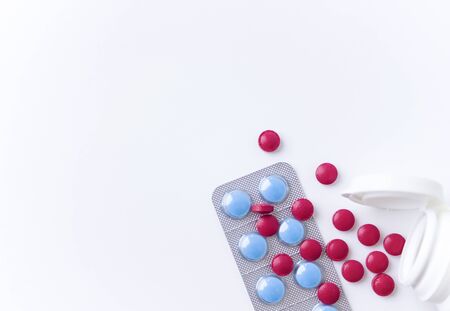 Red and blue pills on white background. Scattered red tablets from a plastic jar next to blue...