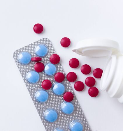 Red and blue pills on white background. Scattered red tablets from a plastic jar next to blue tablets in blistersの写真素材
