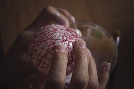 Christmas toys with their own hands made of thread and glue. The girl makes a ball of red thread on...