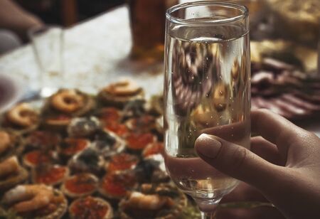 A woman holds a glass of sparkling champagne against the background of a festive table. A glass of...