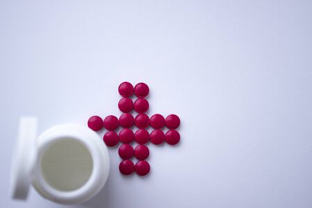 The tablets are arranged in the shape of a cross. Red tablets with a plastic jar. The concept of health. Help with recovery. Red cross.の写真素材