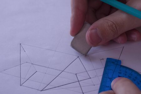 A man draws a diagram with a ruler, eraser and pencil. Design and create a project on a white sheet of paper close-up.の写真素材