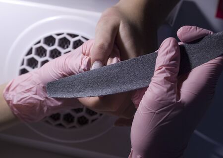 A manicurist saws nails with a nail file against the background of a vacuum cleaner. Giving a square shape to the nails. Professional manicure in the salon close-up.の写真素材