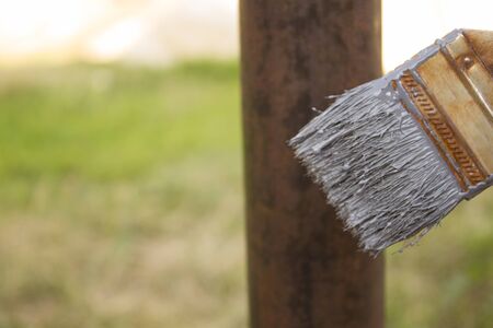 Paint brush and iron post on the background of grass. Brush with gray paint for painting a metal column in the summer. Corrosion on the post.の写真素材