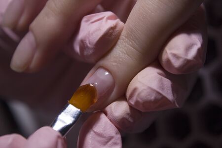 The manicurist applies a base layer to the client's nail.Applying a transparent varnish with a...