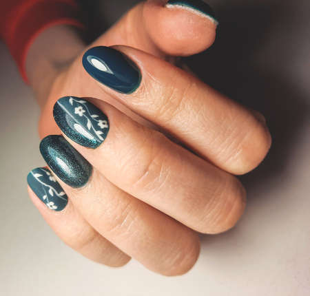 Fashionable emerald gel nail polish with a shiny design and white twigs. Manicure of dark green...