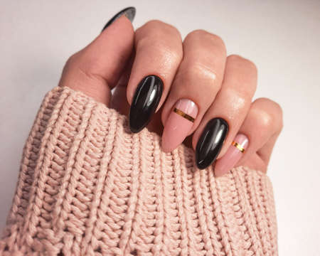 Beautiful two-tone manicure with gold design. Hands in a sweater with black and camouflage gel polish. Stylish nail polish coating.の写真素材