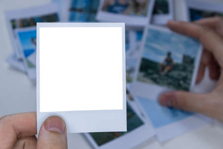 A person holds a photo in his hands against the background of other photos. Photo in hand close-up. A person looks at a photo from a .の写真素材