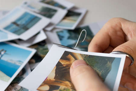 A man cuts out photos with people in close-up. A man uses scissors to cut printed photos for an album. A person holds a photo in his hands against the background of other photos.の写真素材