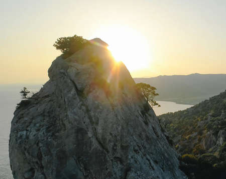 A steep cliff. A steep rocky mountain against a clear sky and a sun glare. A mountain peak with growing trees.の写真素材