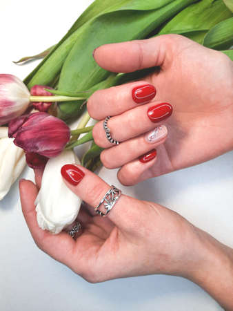 Women's manicure with red gel polish and a beautiful flower design. Women's hands with silver rings and red nails next to rosesの写真素材