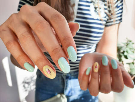 Women's hands with a delicate gel polish of blue and yellow with an ice cream design. Manicure with...