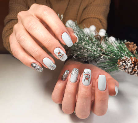A neat manicure with a delicate design in pastel color with a christmas tree branch covered with snow. Long square nails with gel polish and hare design and glittersの写真素材