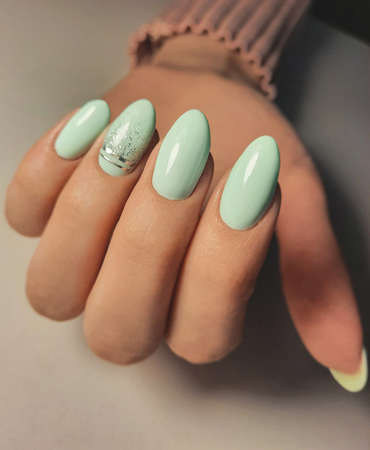Gentle gel polish of pale turquoise color on almond-shaped nails with silver stripes. Nude manicure with shiny stripes design. Pastel color coating on the nails.の写真素材