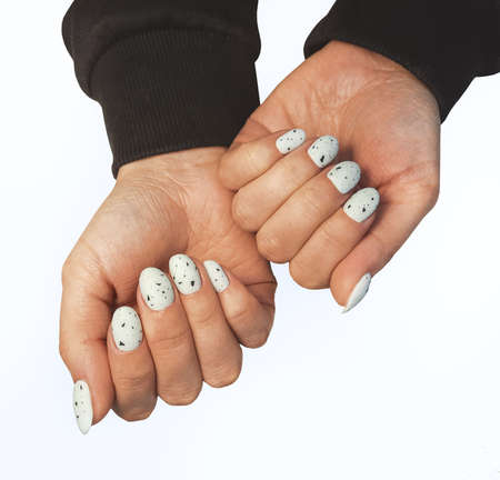 Women`s hands with white gel polish and black fragments on nails. Women's manicure with white lacquer and black abstract design. Quail egg designの写真素材