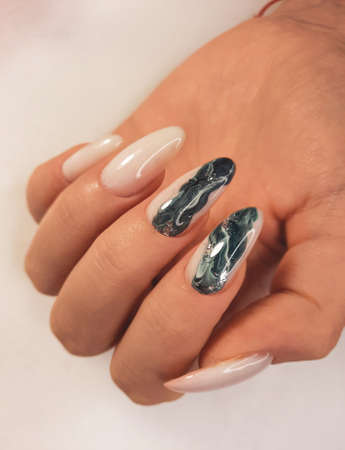 Gentle camouflage gel polish on long nails with a wavy abstract design. Nude manicure with a beautiful green-gray design. Pastel color coating on the nails with a fluid abstract design.の写真素材