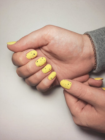 Women`s hands with pale yellow gel polish and black fragments on nails. Women's manicure with yellow lacquer and black abstract design. Quail egg designの写真素材