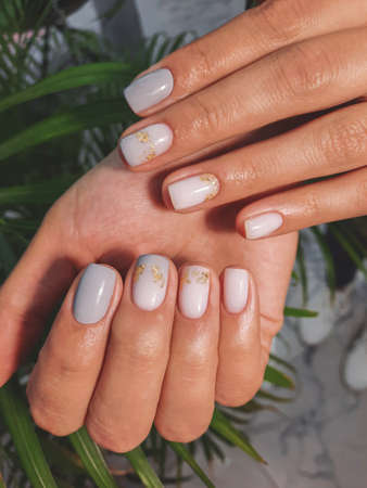 Women's hands with gray-beige manicure and gold design. Beautiful nails covered with gradient gel...